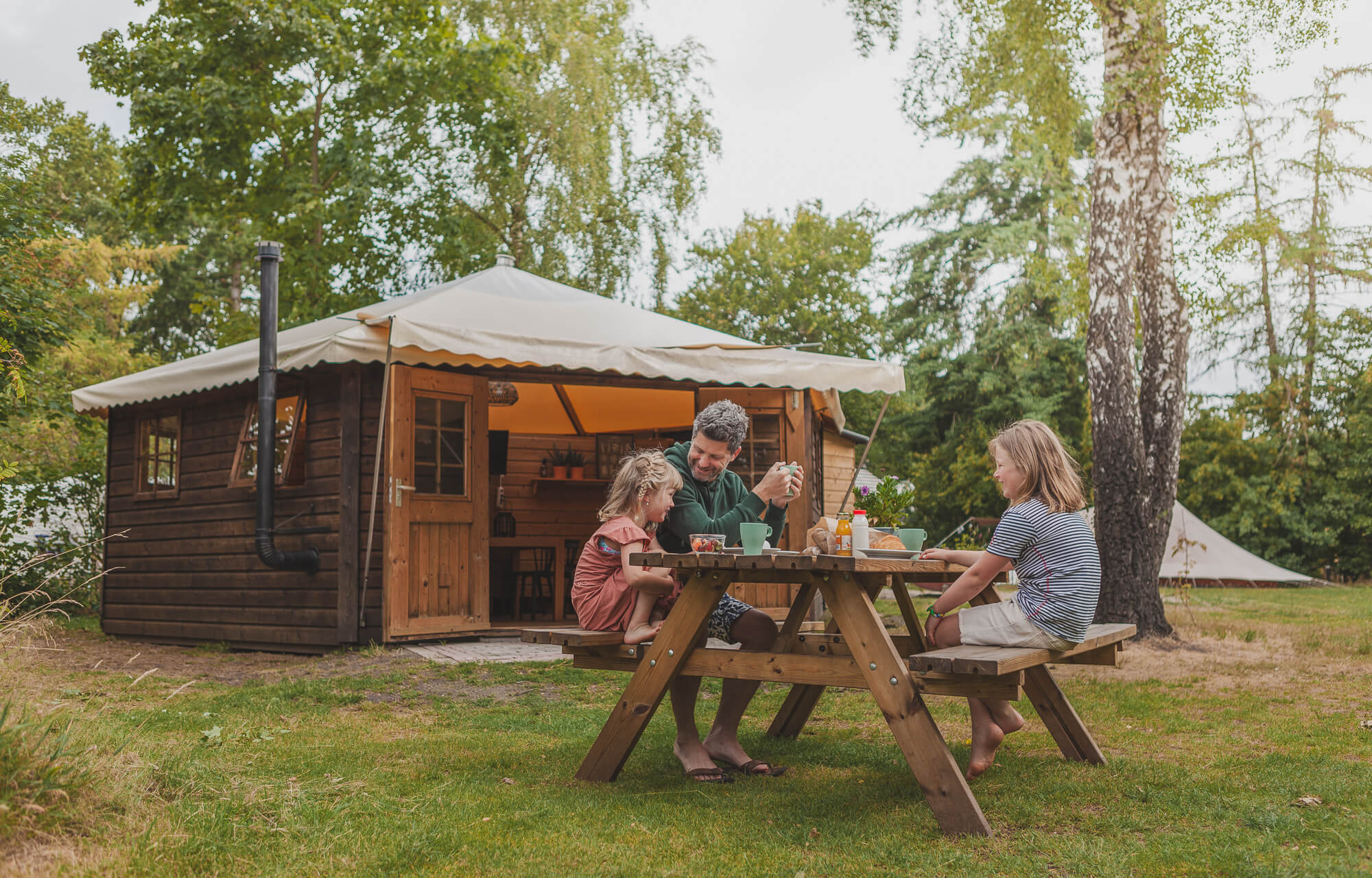 Gezin aan picknicktafel voor Boslodge bij Lemeler Esch natuurcamping in Overijssel