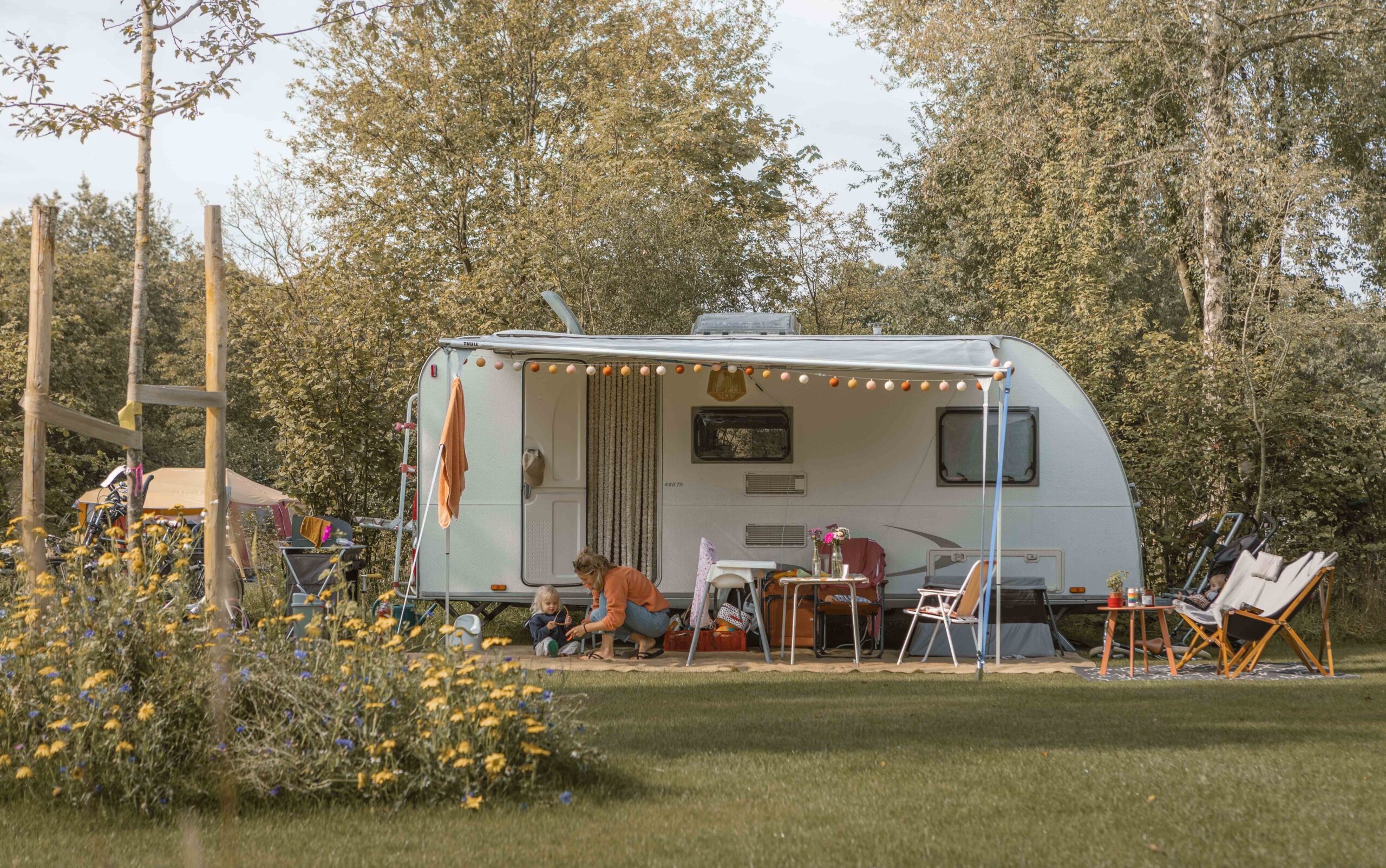 Moeder en peuter voor de caravan op kampeerveld Boomgaard bij Lemeler Esch natuurcamping